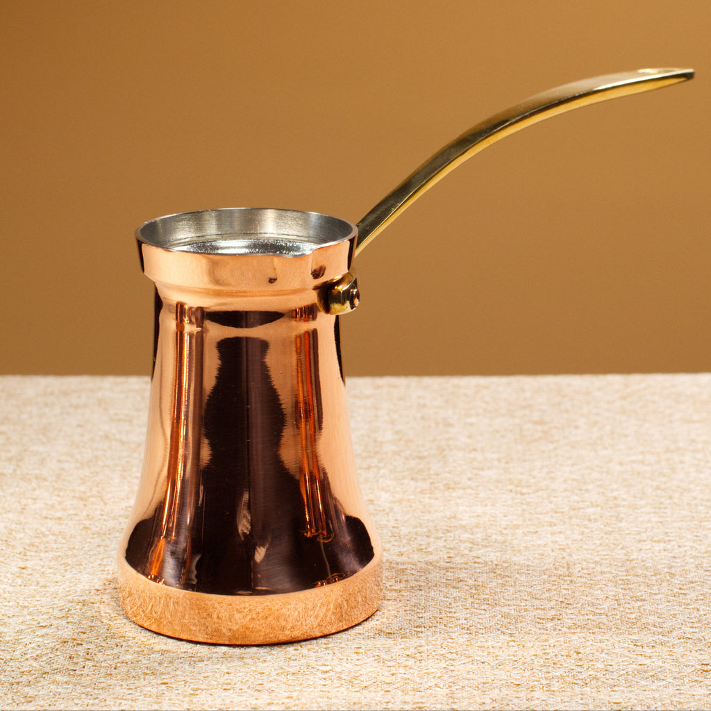 Copper coffee pot with a gold handle on a textured surface with a brown background