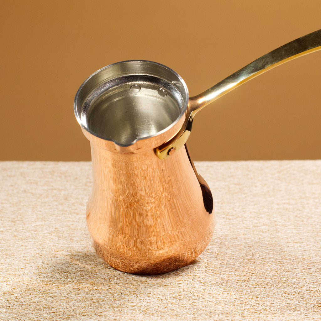Copper coffee pot with a gold handle on a textured surface with a brown background