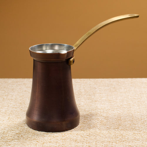 Traditional Turkish coffee pot with a brass handle on a textured surface and brown background