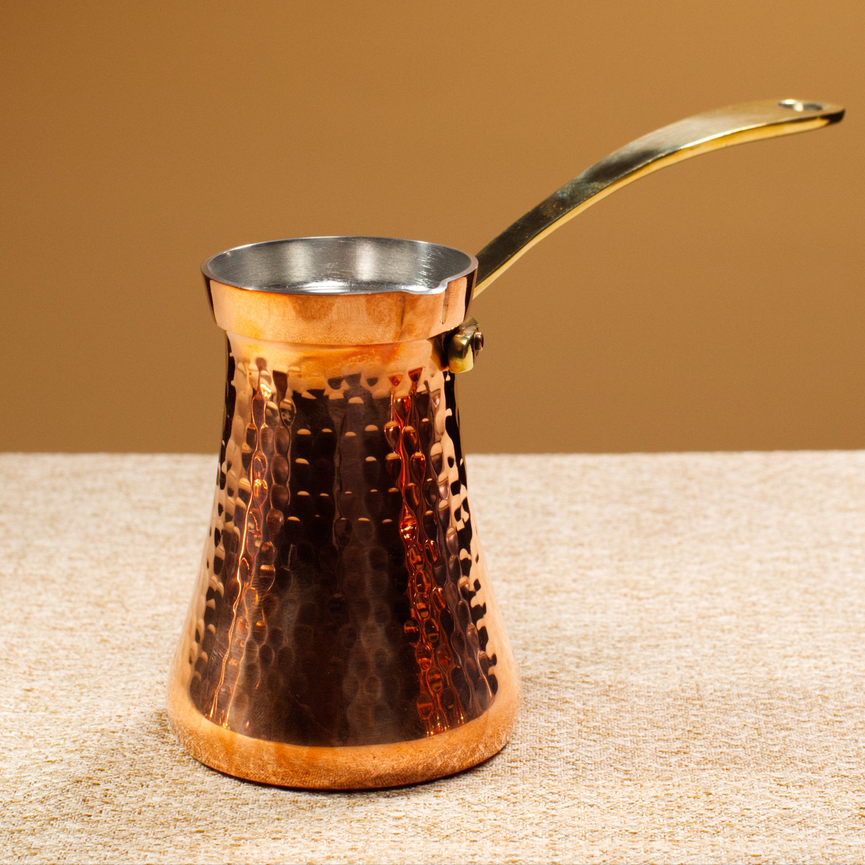 Copper coffee pot with a gold handle on a textured surface with a brown background