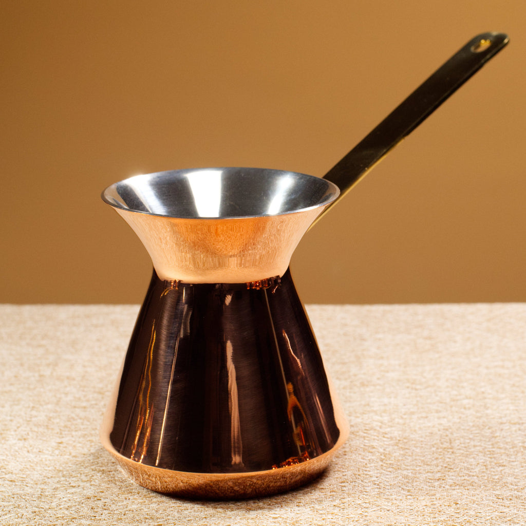 Copper coffee pot with a brass handle on a textured surface with a brown background